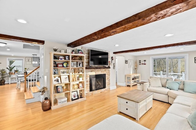 living room featuring beamed ceiling, a stone fireplace, and light wood-type flooring