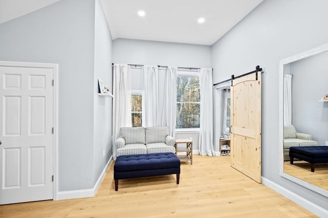 sitting room with a towering ceiling, a barn door, and light hardwood / wood-style flooring