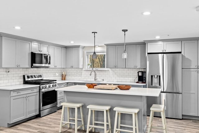 kitchen featuring a breakfast bar, sink, decorative backsplash, hanging light fixtures, and stainless steel appliances