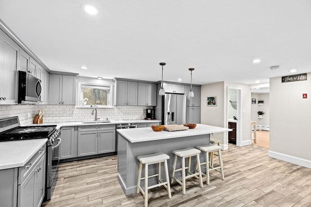 kitchen with sink, hanging light fixtures, stainless steel appliances, a center island, and light hardwood / wood-style floors