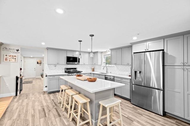 kitchen featuring gray cabinets, a kitchen breakfast bar, hanging light fixtures, a center island, and stainless steel appliances