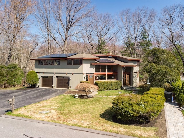 view of front of home featuring roof mounted solar panels, a front lawn, driveway, and a garage