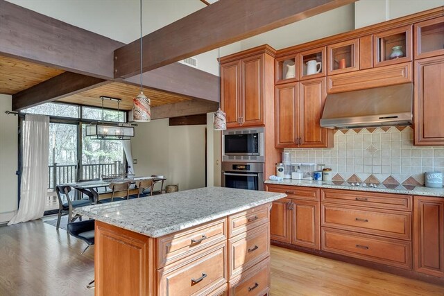 kitchen with brown cabinetry, stainless steel appliances, beamed ceiling, wall chimney range hood, and backsplash