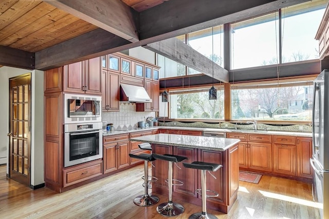 kitchen featuring tasteful backsplash, appliances with stainless steel finishes, a kitchen island, range hood, and light wood finished floors