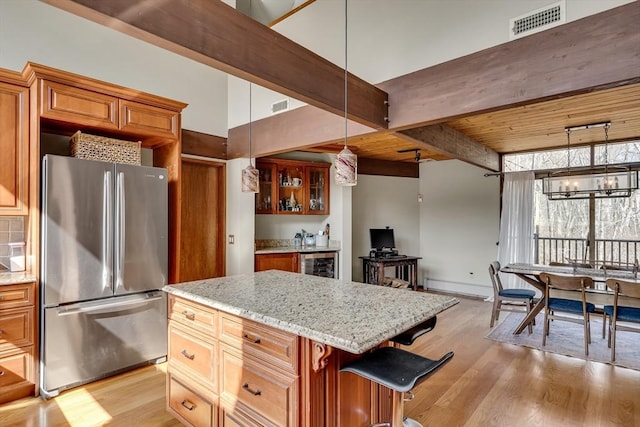 kitchen with light stone counters, light wood-style flooring, beverage cooler, visible vents, and freestanding refrigerator