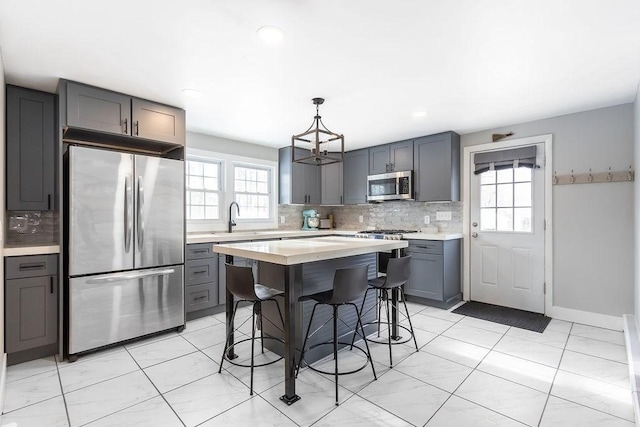 kitchen featuring gray cabinets, a kitchen island, appliances with stainless steel finishes, decorative light fixtures, and a kitchen breakfast bar