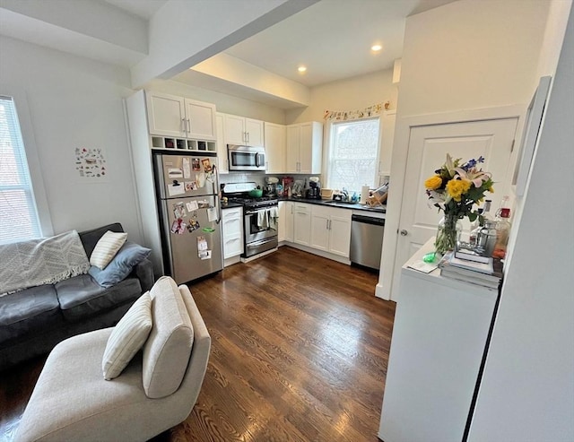 kitchen featuring stainless steel appliances, open floor plan, a sink, white cabinets, and dark wood-style flooring