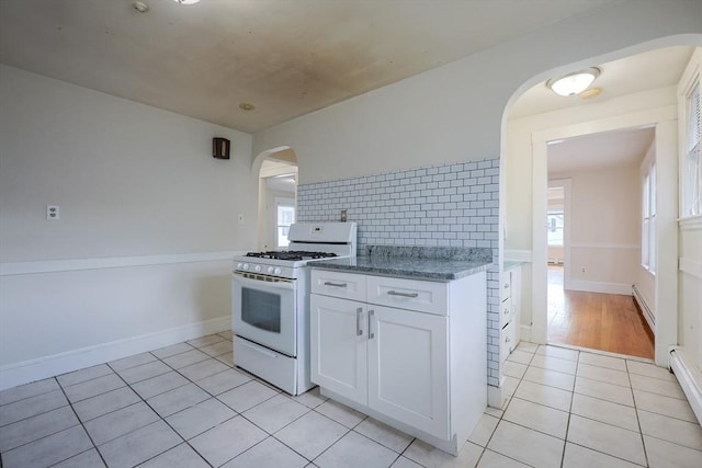 18-20 Melbourne Ave, Newton, MA 02460 - kitchen featuring white gas range oven, arched walkways, light tile patterned flooring, white cabinets, and tasteful backsplash
