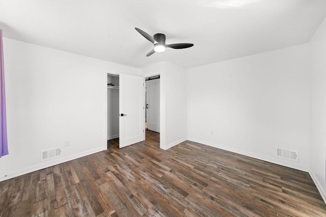 unfurnished bedroom featuring ceiling fan, a barn door, and dark hardwood / wood-style flooring