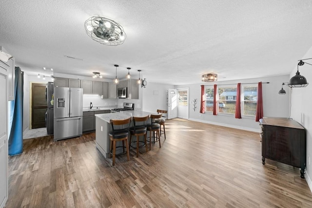 kitchen with gray cabinets, appliances with stainless steel finishes, decorative light fixtures, a breakfast bar, and sink