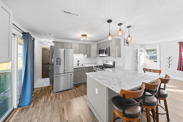 kitchen featuring appliances with stainless steel finishes, sink, hanging light fixtures, a kitchen breakfast bar, and gray cabinetry