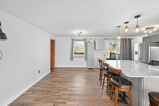 kitchen featuring decorative light fixtures, high end fridge, a kitchen breakfast bar, a textured ceiling, and light stone counters