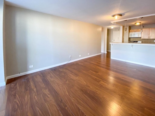 unfurnished living room featuring dark wood-type flooring and baseboards