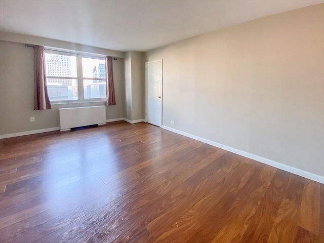 spare room with radiator, baseboards, and wood finished floors