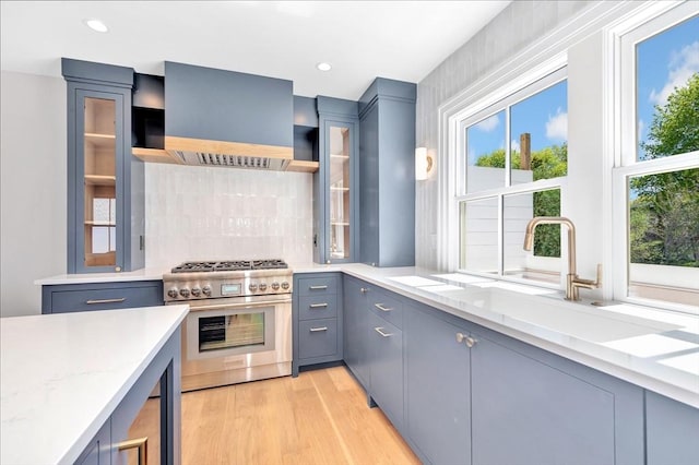 kitchen with wall chimney range hood, light wood-type flooring, gray cabinets, tasteful backsplash, and high end stainless steel range oven