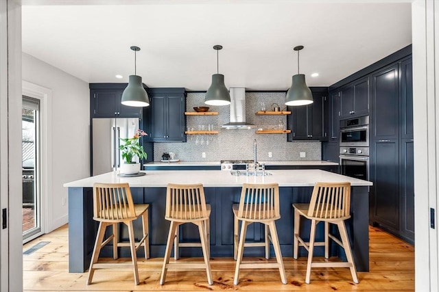 kitchen featuring wall chimney exhaust hood, stainless steel appliances, light countertops, open shelves, and a sink