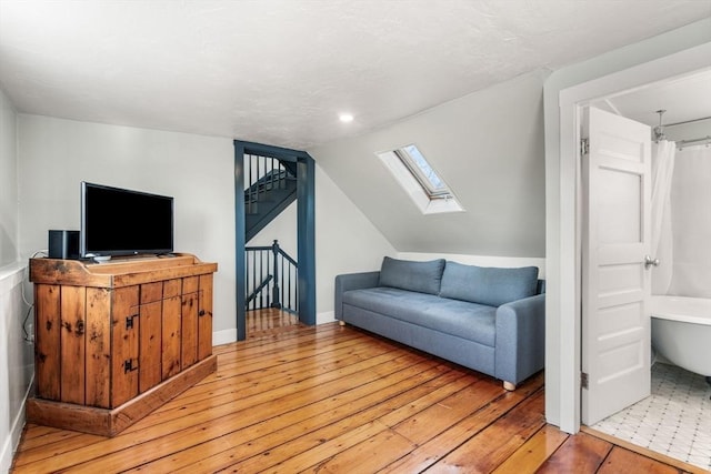 living room with stairway, lofted ceiling with skylight, and light wood-style flooring