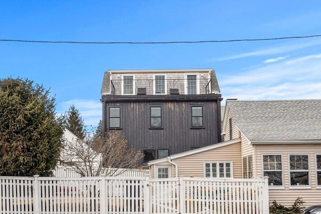 view of front facade featuring roof with shingles, fence, and a balcony