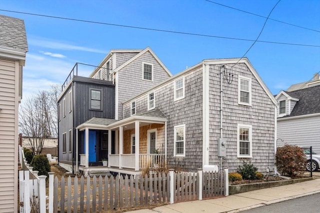 view of front of property featuring a fenced front yard, a porch, and a shingled roof