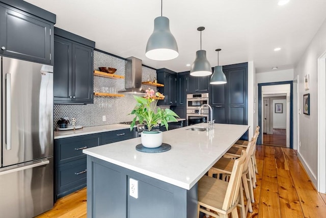 kitchen featuring stainless steel appliances, a sink, wall chimney exhaust hood, backsplash, and open shelves