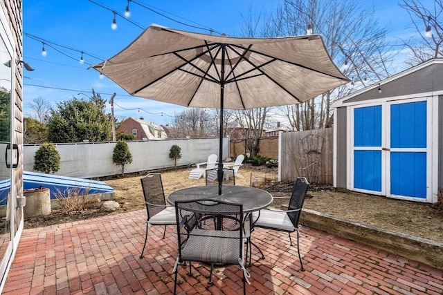 view of patio featuring a storage shed, a fenced backyard, outdoor dining space, and an outbuilding