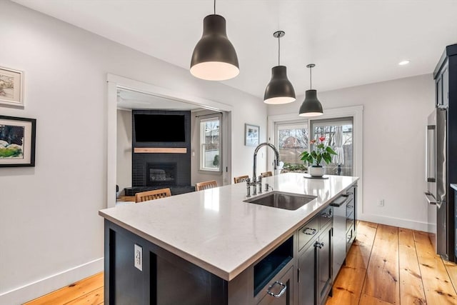 kitchen with an island with sink, light wood-style floors, baseboards, and a sink