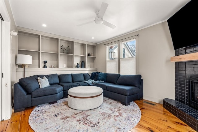 living room with hardwood / wood-style flooring, a fireplace, visible vents, a ceiling fan, and ornamental molding