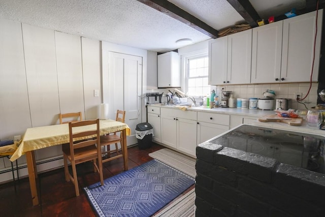 kitchen with light countertops, white cabinets, a textured ceiling, beamed ceiling, and tasteful backsplash