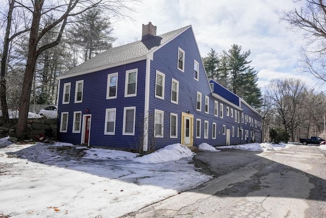 view of snowy exterior with a chimney and a shingled roof