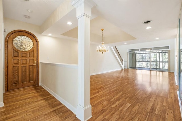 interior space featuring a raised ceiling, wood finished floors, visible vents, and decorative columns