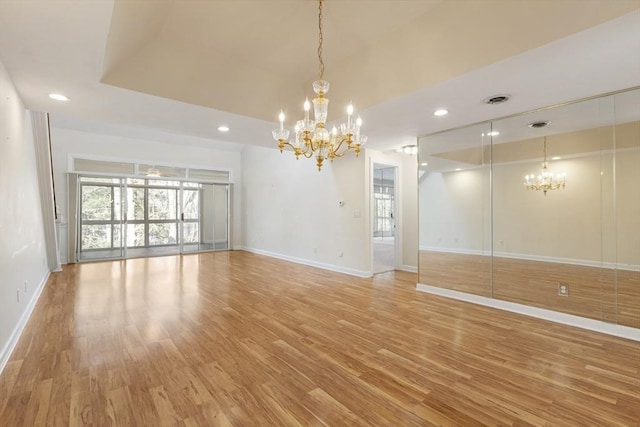 unfurnished room featuring a chandelier, recessed lighting, baseboards, light wood finished floors, and a raised ceiling