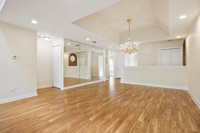 spare room featuring a notable chandelier, recessed lighting, baseboards, light wood-type flooring, and a tray ceiling