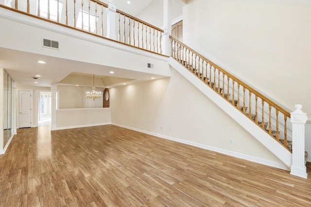 unfurnished living room with a chandelier, wood finished floors, visible vents, and baseboards