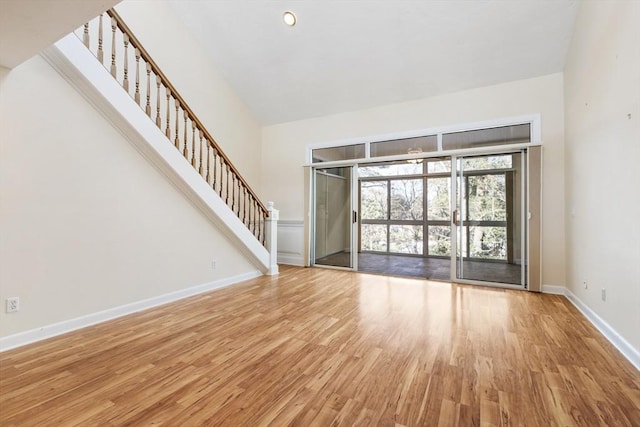 unfurnished living room with baseboards, stairway, a high ceiling, and wood finished floors