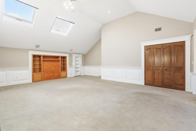 additional living space featuring a wainscoted wall, visible vents, a decorative wall, lofted ceiling with skylight, and carpet flooring