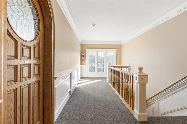 hall featuring a decorative wall, carpet flooring, an upstairs landing, wainscoting, and crown molding