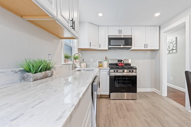 kitchen featuring light stone countertops, white cabinets, appliances with stainless steel finishes, light hardwood / wood-style floors, and sink