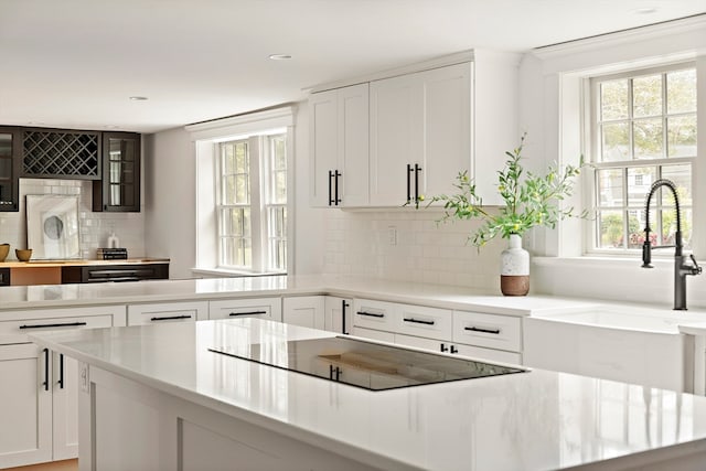 kitchen with black electric cooktop, decorative backsplash, white cabinetry, and sink