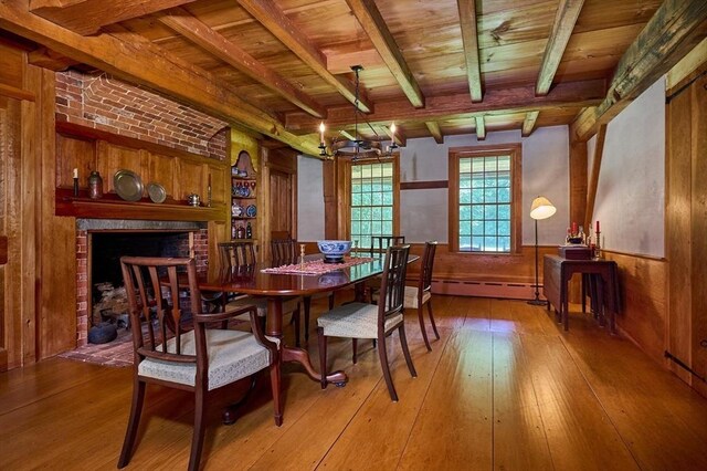 dining area with wooden ceiling, light wood-type flooring, a baseboard heating unit, wood walls, and a brick fireplace