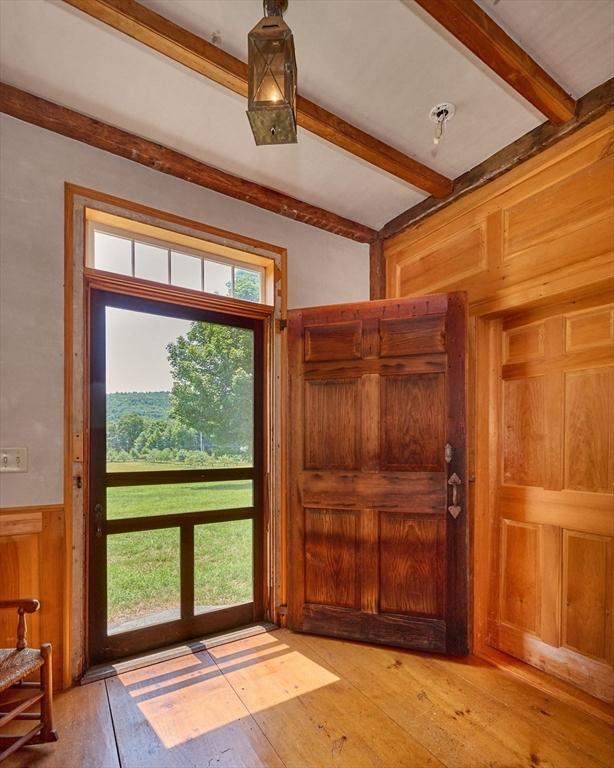 entryway with beamed ceiling, wood walls, and light wood-type flooring