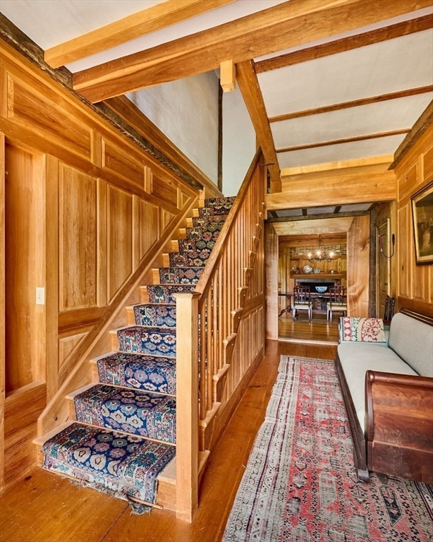 stairs with wooden walls, hardwood / wood-style floors, and beam ceiling