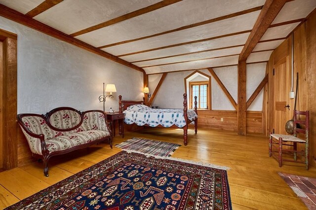 bedroom featuring beamed ceiling, light hardwood / wood-style flooring, and wooden walls