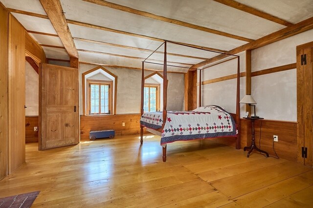 unfurnished bedroom featuring wood walls, beam ceiling, and light wood-type flooring