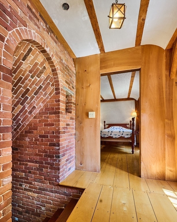 hallway with brick wall, beamed ceiling, and hardwood / wood-style floors