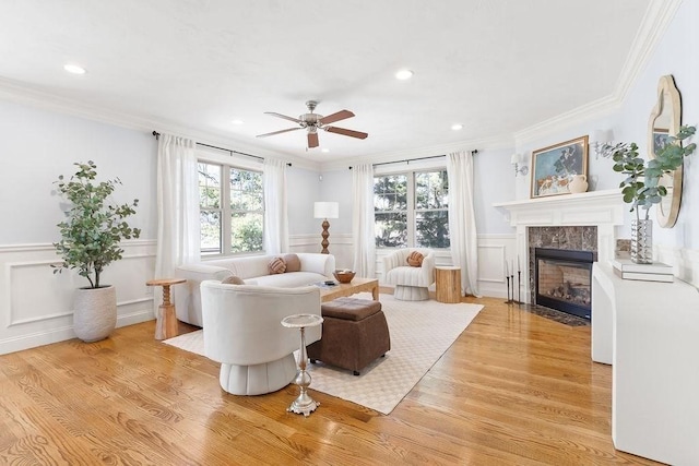 living room featuring a wainscoted wall, light wood finished floors, a high end fireplace, and crown molding