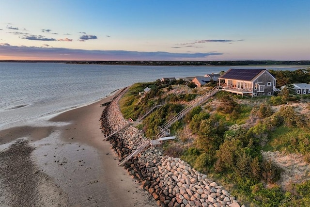 aerial view at dusk with a water view and a beach view