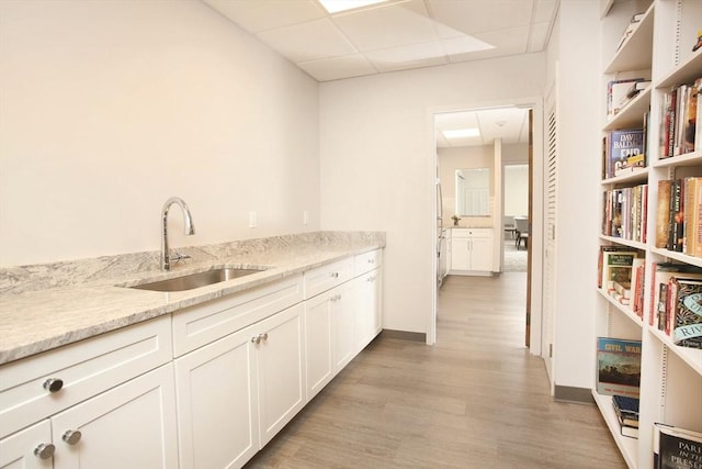 210 Nahanton St Unit 504, Newton, MA 02459 - kitchen featuring a sink, a drop ceiling, light wood-type flooring, white cabinets, and light stone counters