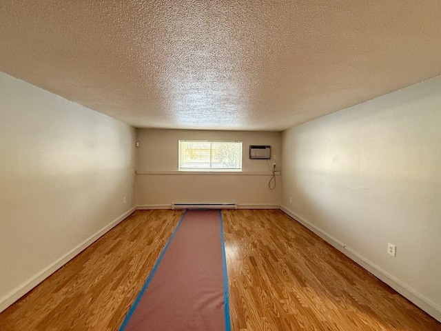 empty room featuring baseboard heating, a wall unit AC, a textured ceiling, and hardwood / wood-style floors