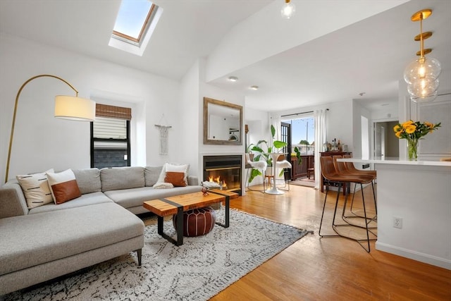 living room featuring vaulted ceiling with skylight and light wood-type flooring