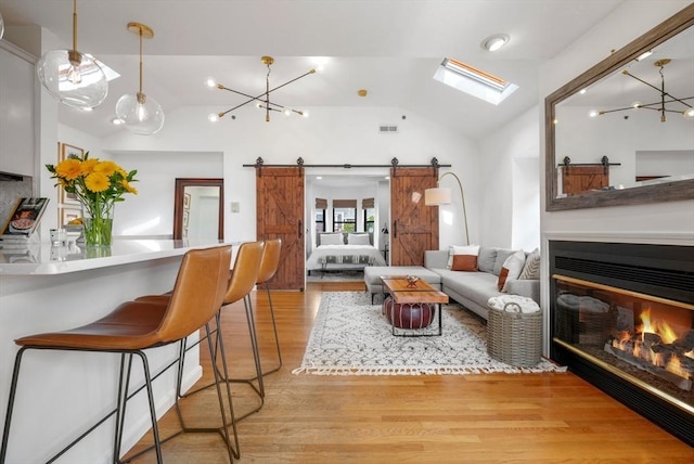 living room with light hardwood / wood-style flooring, vaulted ceiling with skylight, and a barn door